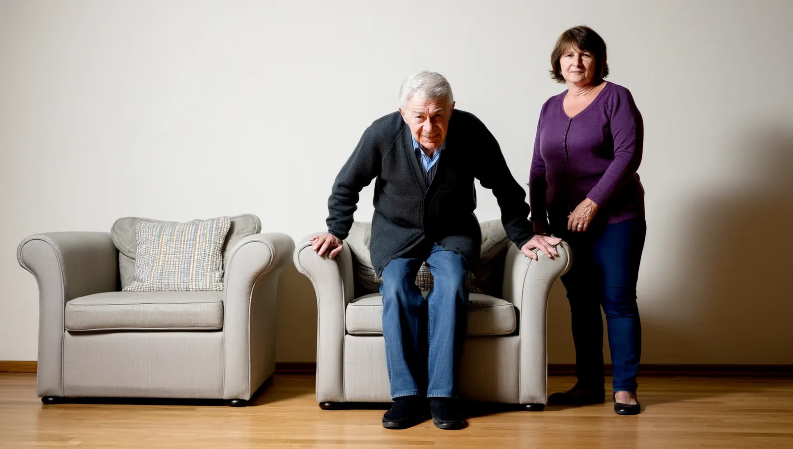 Older man rising from an armchair, woman beside him