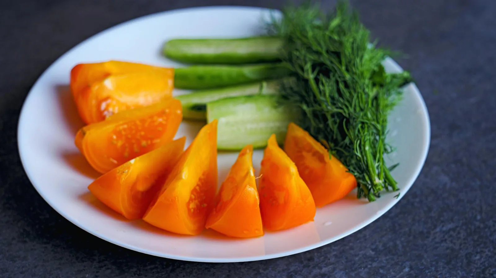 A healthy plate of sliced yellow bell peppers, cucumbers, and fresh dill.