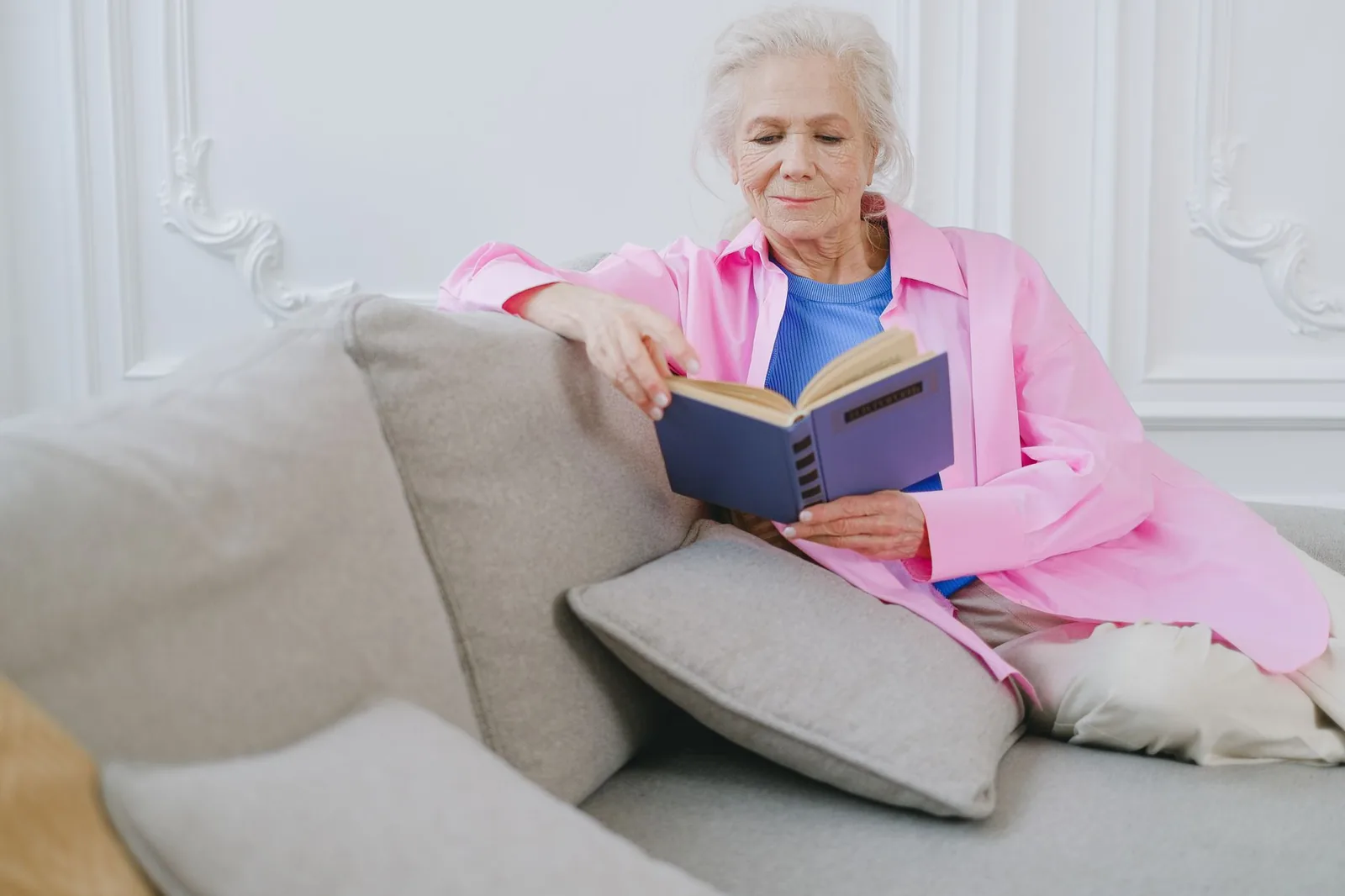An older woman reading a hardback book on a sofa