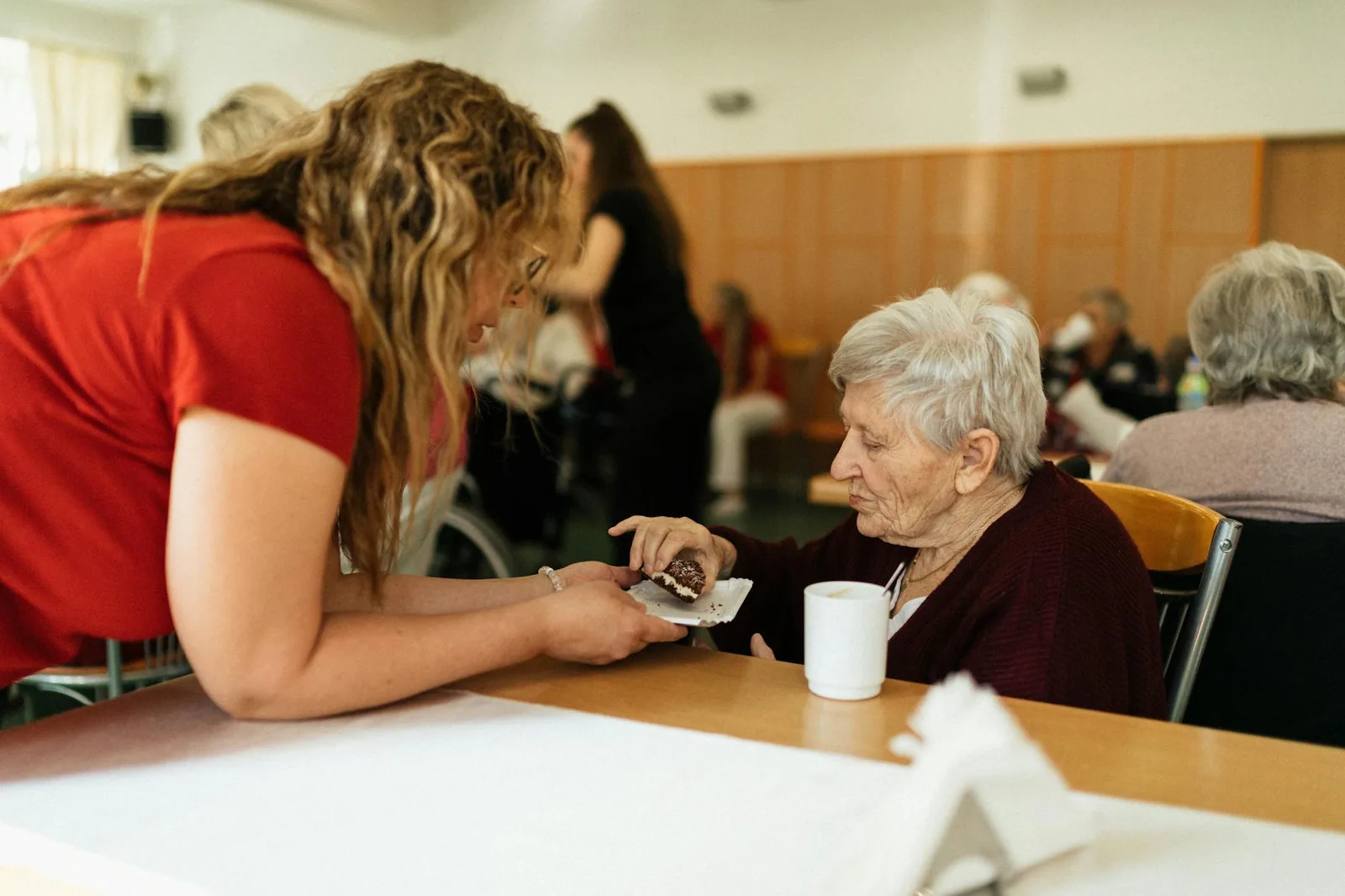 An elderly woman being warmly assisted by a caregiver in a senior living community.