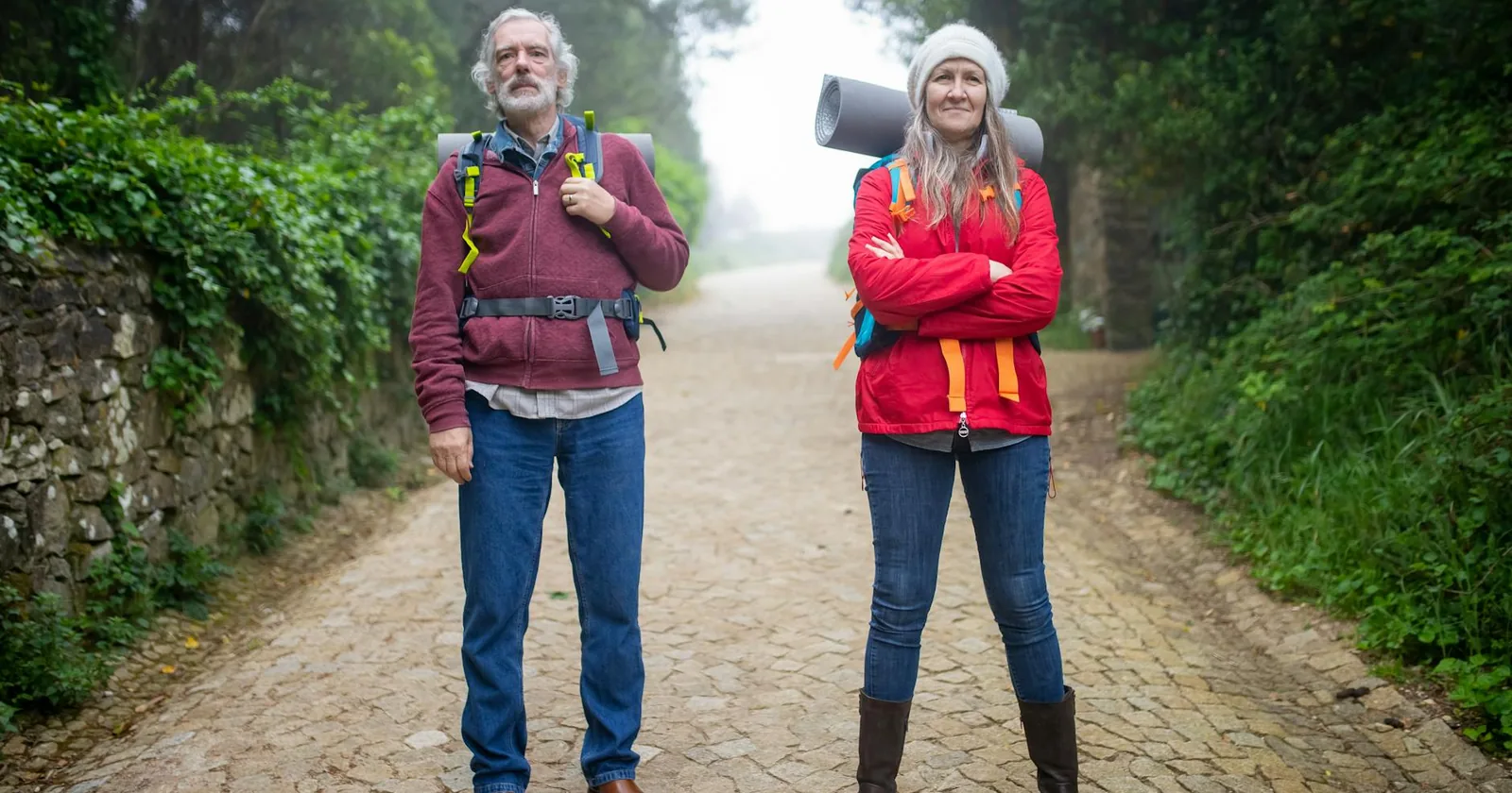 Active senior couple walking along a cobblestone path surrounded by lush greenery.