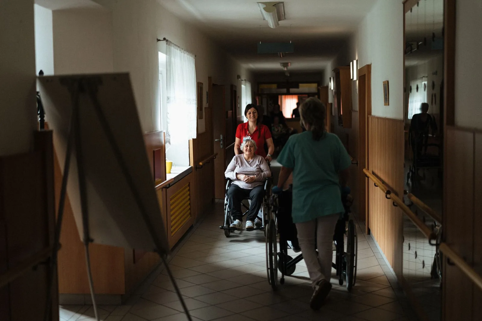 Caregiver pushing a woman in a wheelchair down a hallway