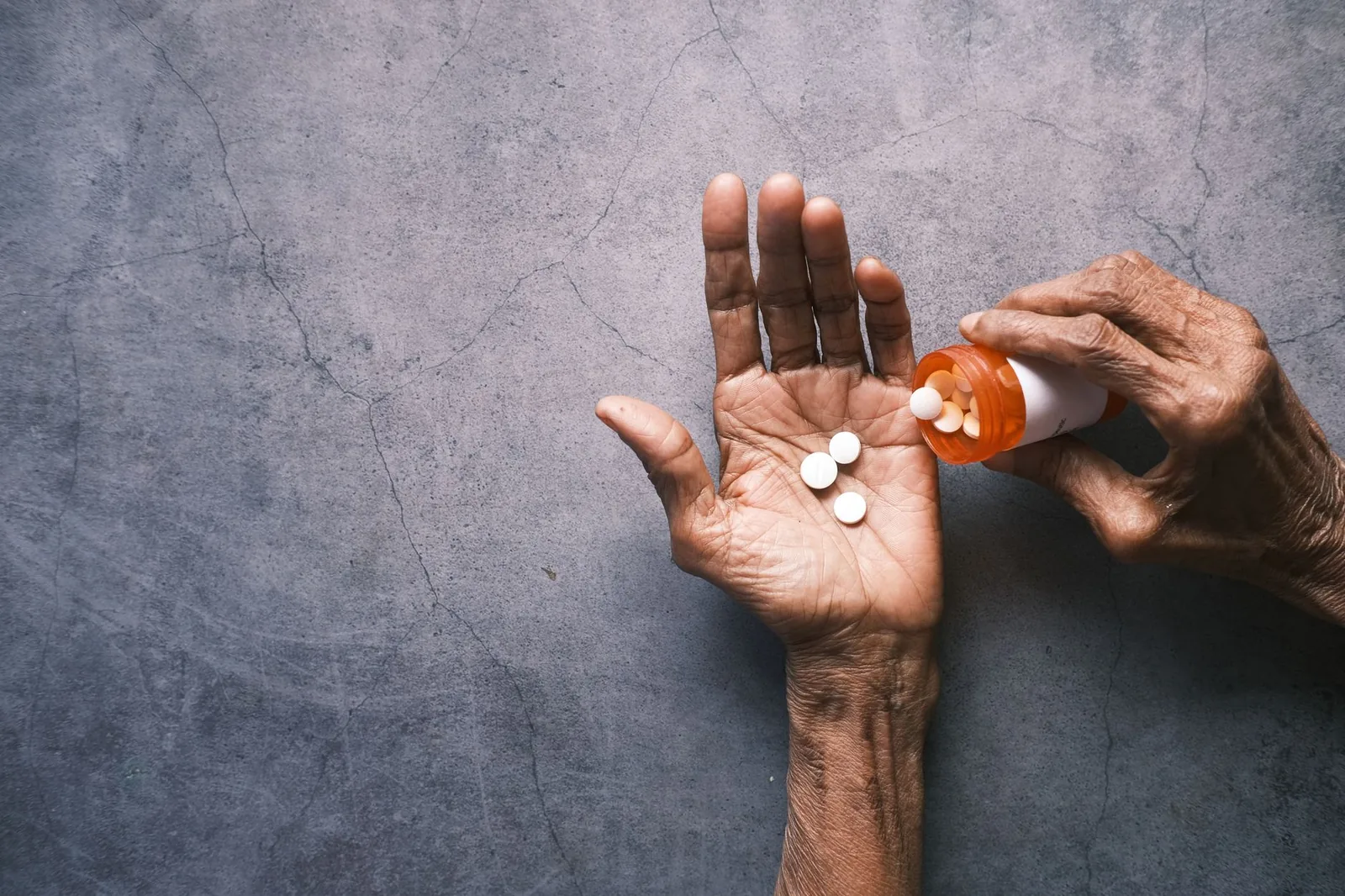 Elderly person's hand pouring pills from a bottle