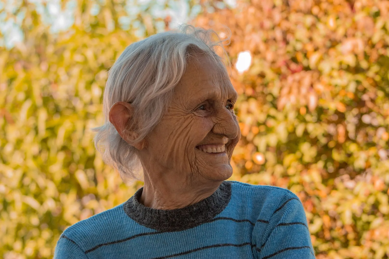 Portrait of a smiling elderly woman outdoors with autumn leaves.