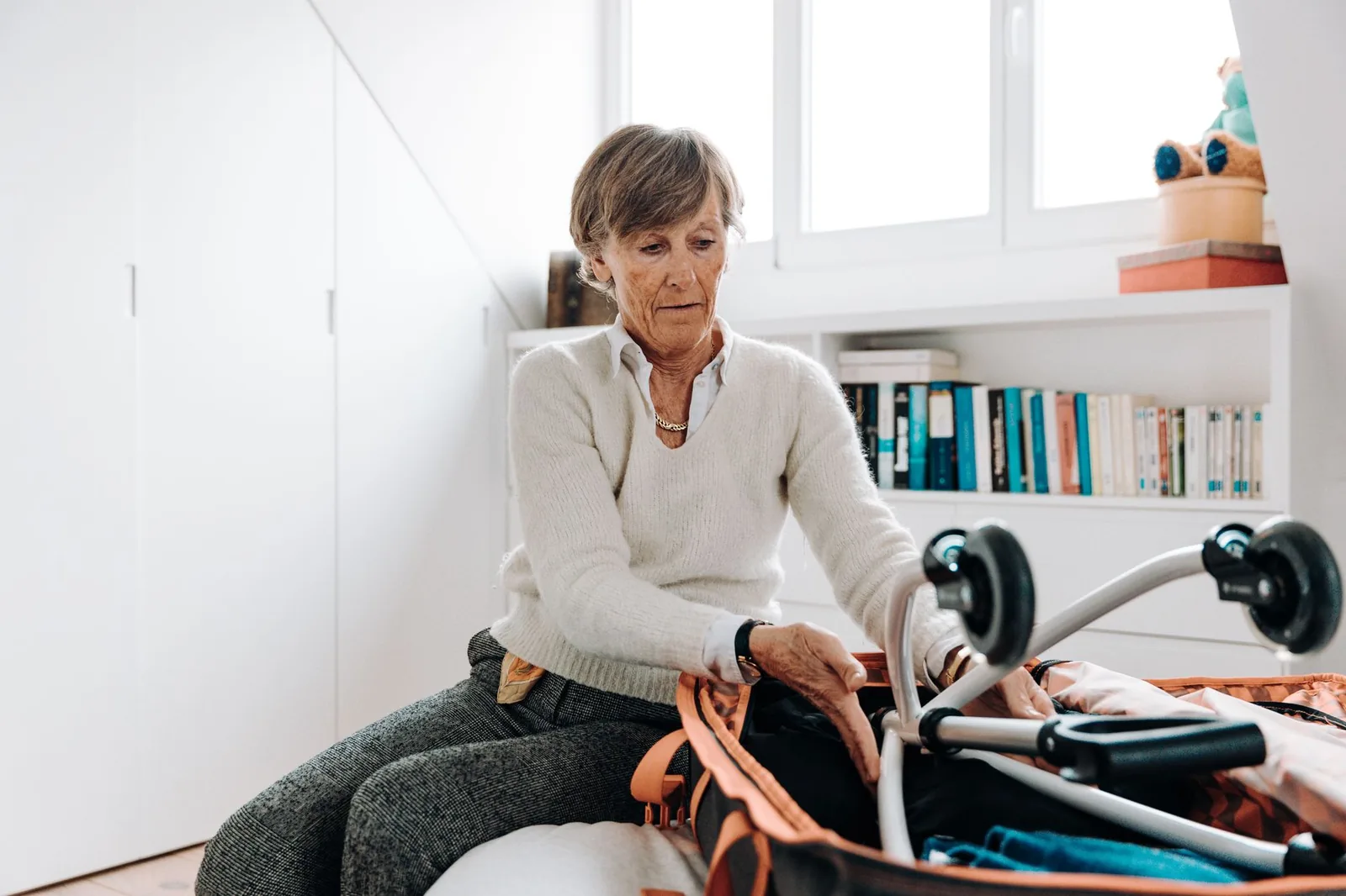 Older woman packing an open suitcase beside a rollator
