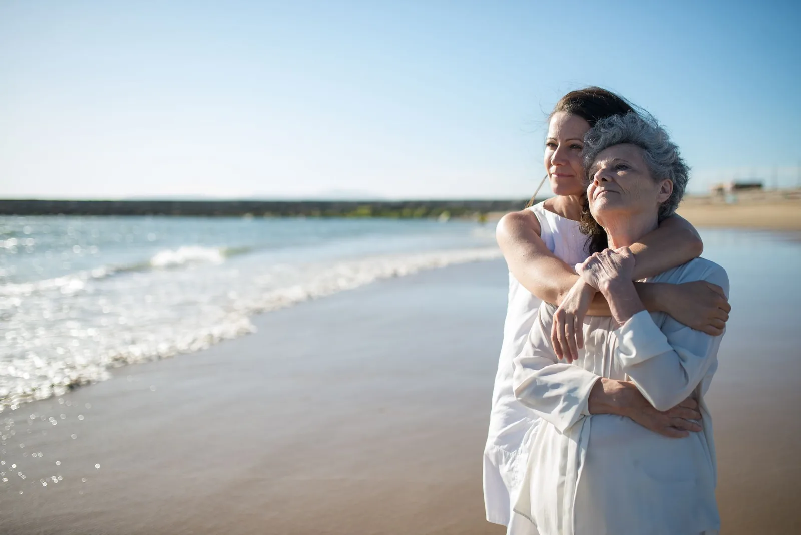An elderly mother and her adult daughter sharing a warm embrace outdoors.