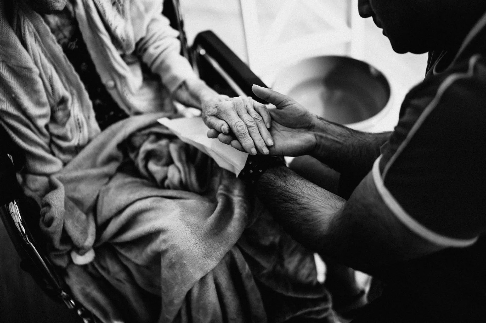 A caregiver holding the hands of an elderly woman seated in a wheelchair.