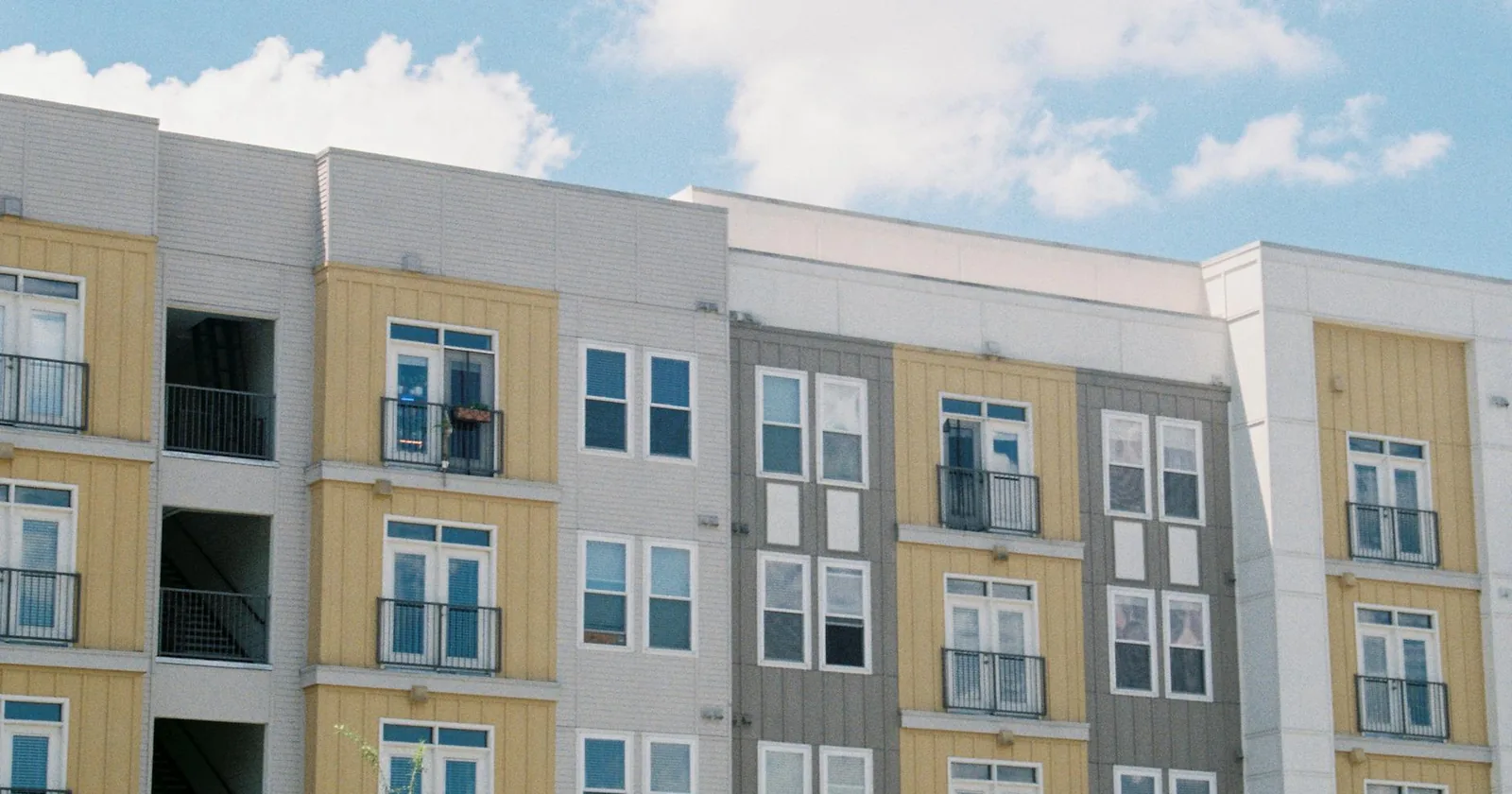 Modern senior living apartment building with yellow and grey panels rising against a clear blue sky, signaling the new construction families increasingly compete for.