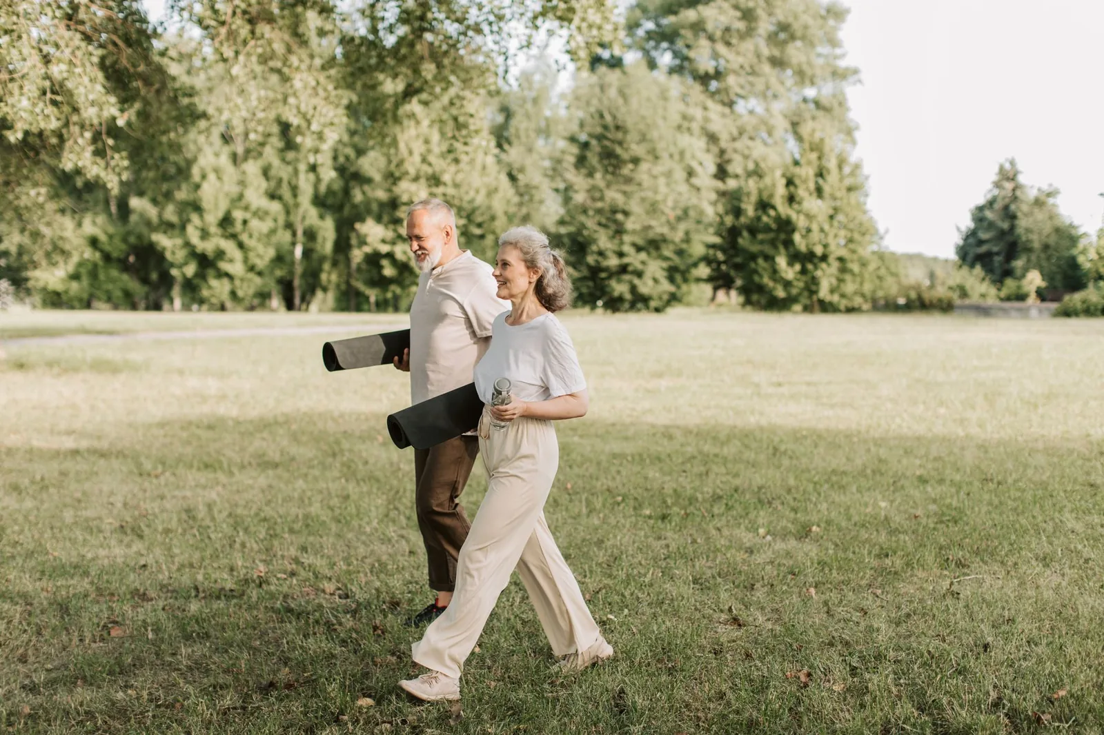 An older couple walking across grass with yoga mats