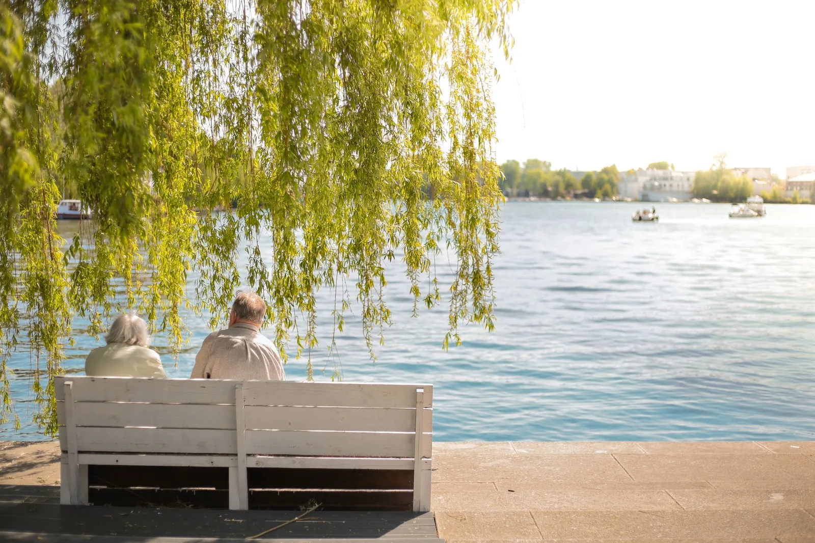 An older couple sitting on a bench facing a lake