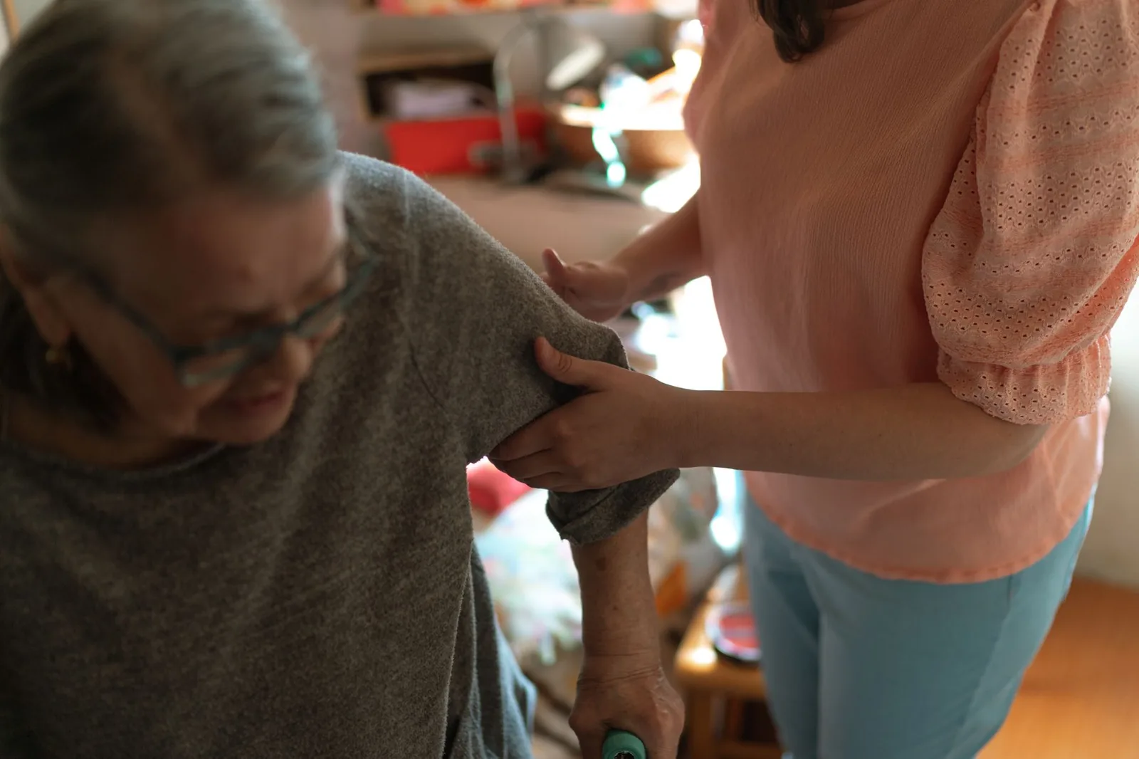 A caregiver steadying an older woman by the arm as she stands with a walker in her own home.